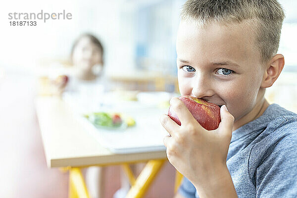 Schüler isst in der Mittagspause in der Cafeteria frischen Apfel