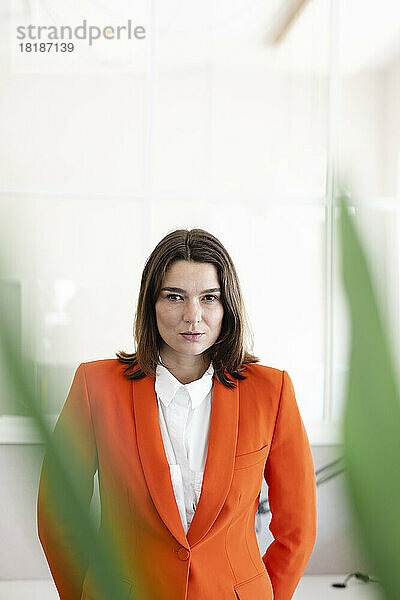 Selbstbewusste Geschäftsfrau mit orangefarbenem Blazer im Büro