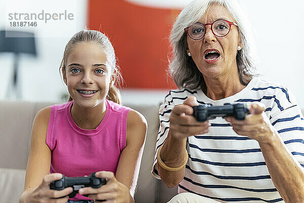 Konzentrierte Großmutter und Enkelin spielen zu Hause Videospiel mit Joysticks