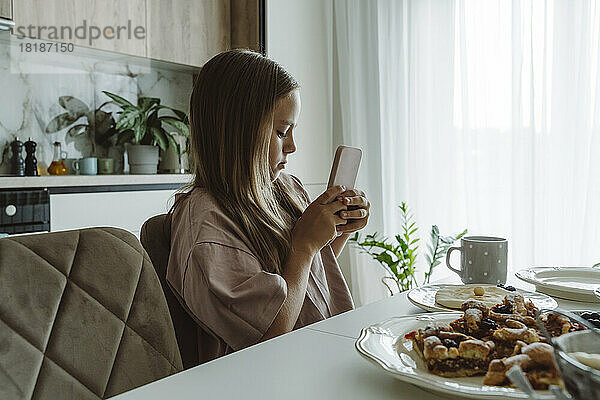 Mädchen fotografiert das Frühstück auf dem Tisch mit dem Smartphone zu Hause