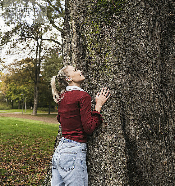 Junge Frau steht am Baum im Park