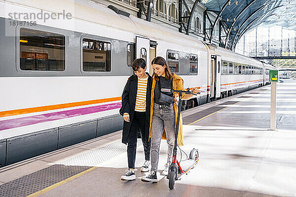 Lächelnde Freunde  die mit dem Tretroller am Bahnhof spazieren gehen