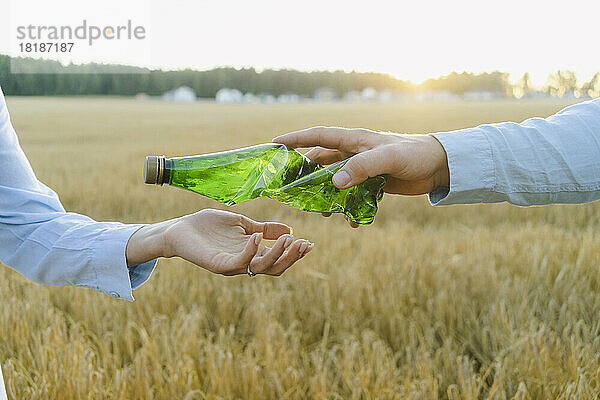 Hand eines Mannes  der einer Frau auf dem Feld eine zerknitterte Plastikflasche reicht
