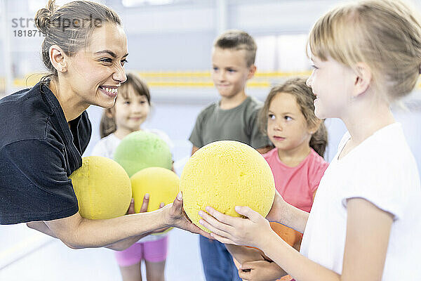 Glücklicher Lehrer  der dem Schüler auf dem Schulsportplatz Ball gibt