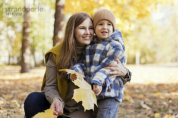 Netter Junge mit Mutter hält gelbe Blätter im Park