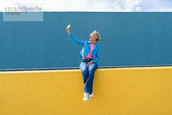 Glückliche reife Frau  die ein Selfie mit dem Handy an der Wand macht