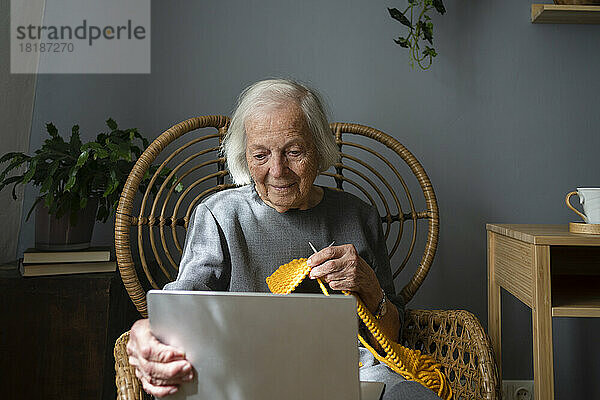 Senior woman learning knitting through laptop at home