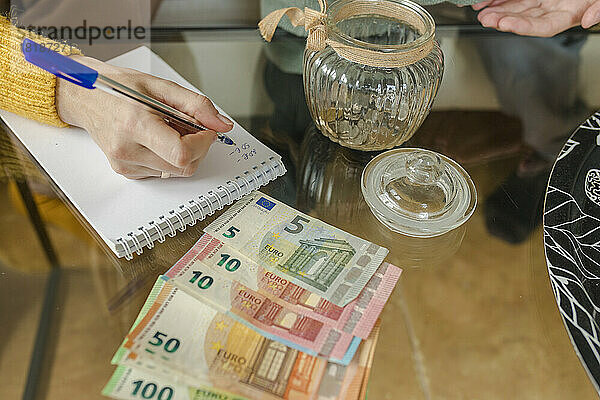 Hand of woman writing on note pad and counting currency at home