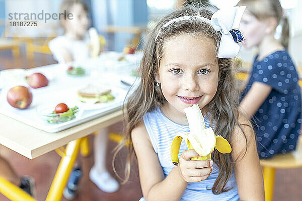 Girl wearing headband holding banana at lunch break in cafeteria