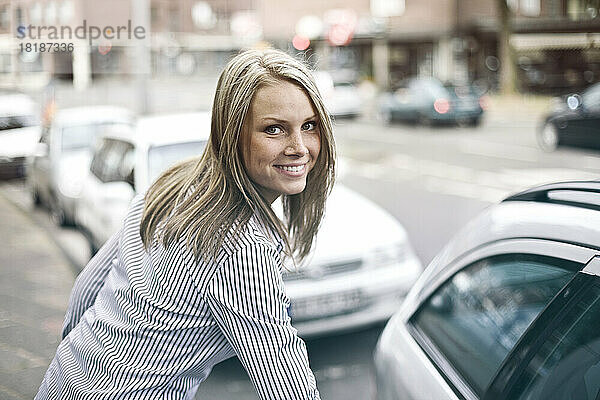 Deutschland  Düsseldorf  junge Frau steigt ins Auto  lächelnd  Porträt
