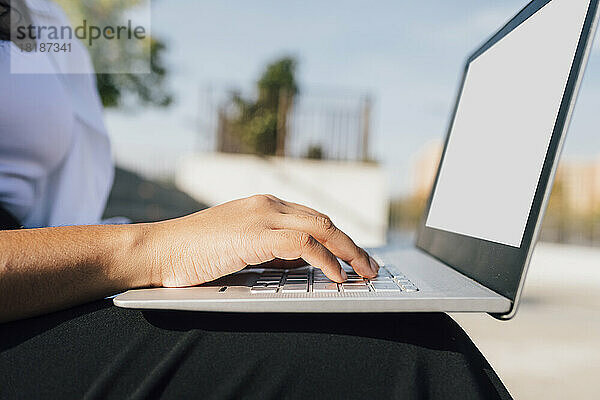 Hand einer Frau  die an einem sonnigen Tag einen Laptop benutzt