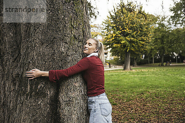 Lächelnde Frau umarmt Baum im Park
