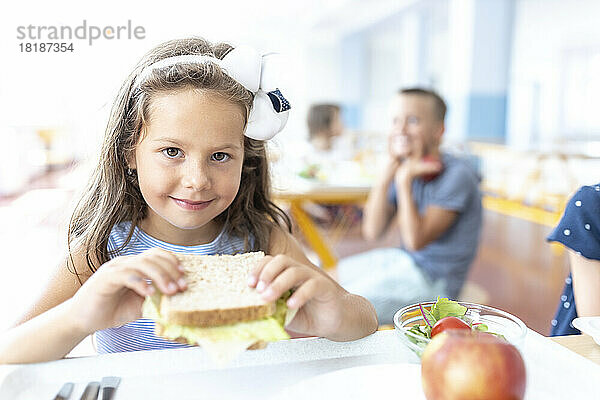 Lächelndes Mädchen hält Sandwich in der Schulcafeteria