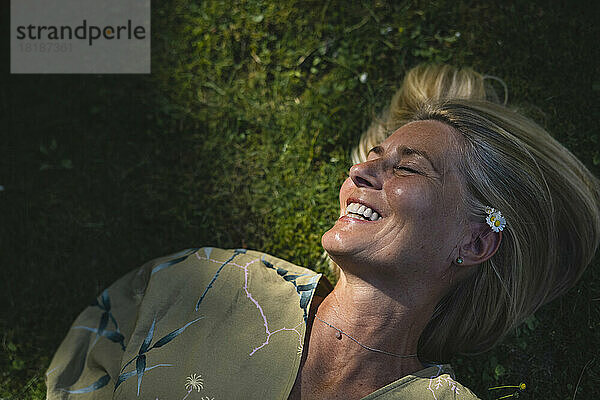 Glückliche reife Frau  die auf Gras liegt und das Sonnenlicht genießt