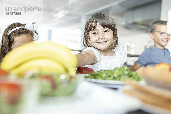 Lächelndes Mädchen  das in der Mittagspause in der Schulcafeteria eine Banane isst