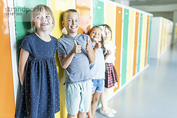 Glückliche Grundschüler stehen neben bunten Schließfächern im Schulkorridor