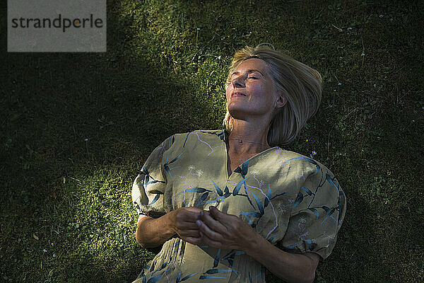 Reife Frau liegt mit geschlossenen Augen im Garten auf Gras