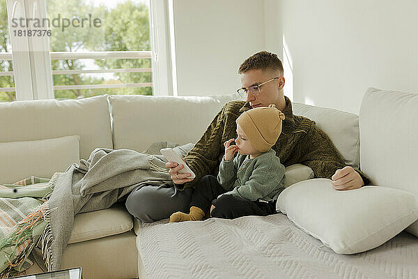 Junger Mann benutzt Smartphone und Sohn sitzt zu Hause auf dem Sofa