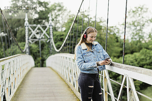 Teenagermädchen benutzt Smartphone und hört Musik auf einer Brücke