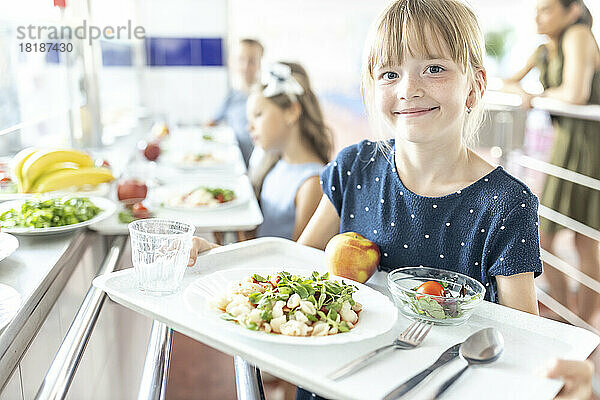 Lächelndes Mädchen hält Essenstablett in der Schulkantine