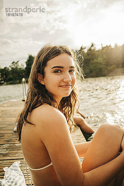 Seitenansicht einer lächelnden Frau  die im Urlaub auf einem Steg am See sitzt