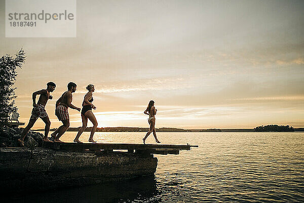 Männliche und weibliche Freunde laufen im Urlaub bei Sonnenuntergang auf dem Steg Richtung See