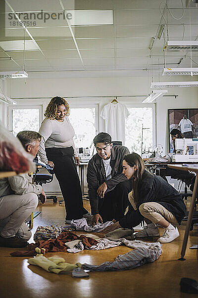 Modedesigner diskutieren miteinander  während sie in einem Workshop recycelte Kleidung auf dem Boden sortieren