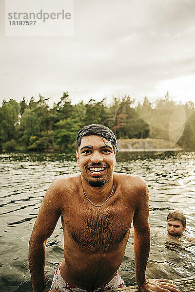 Porträt eines nassen Mannes ohne Hemd  der im Urlaub mit einem männlichen Freund schwimmt