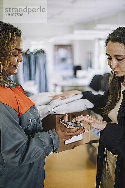 Lächelnde weibliche Lieferperson  die eine digitale Unterschrift von einem Modedesigner entgegennimmt  während sie ein Paket ausliefert