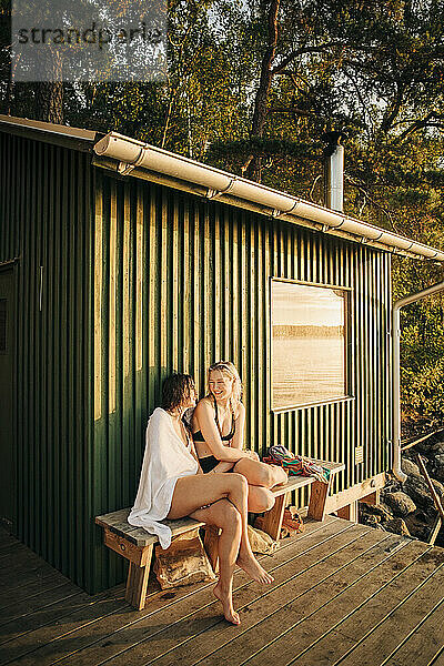 Freundinnen sitzen bei Sonnenuntergang auf einer Bank in der Nähe einer Hütte