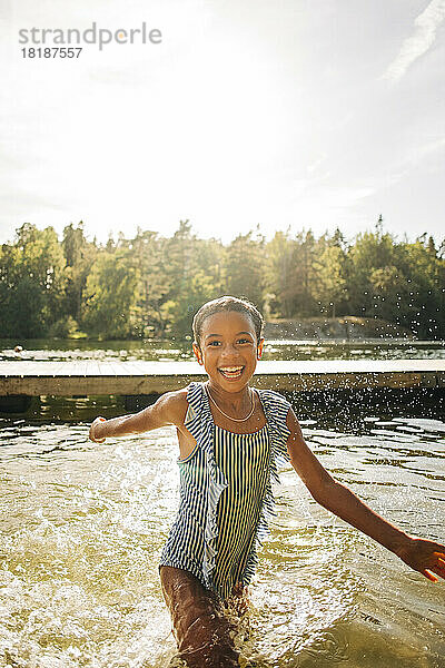 Glückliches Mädchen spielt im See an einem sonnigen Tag im Urlaub