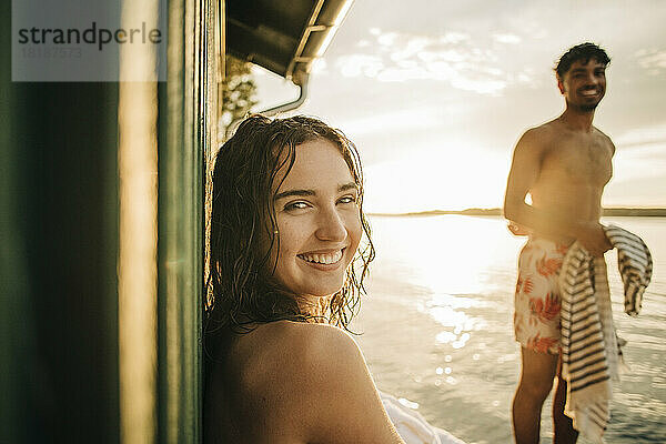 Porträt einer glücklichen Frau  die im Urlaub bei Sonnenuntergang über die Schulter schaut