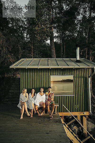 Freunde sitzen auf einer Bank in der Nähe der Hütte am Steg bei Sonnenuntergang