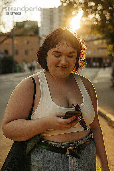 Lächelnde Frau  die bei Sonnenuntergang über ihr Smartphone im Internet surft