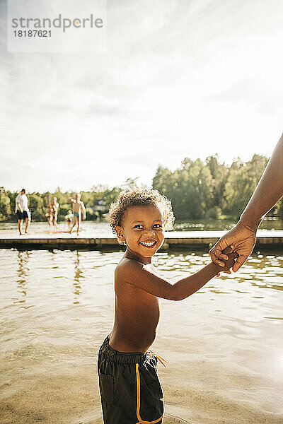 Seitenansicht eines aufgeregten Jungen  der die Hand seiner Mutter hält  während er am See steht