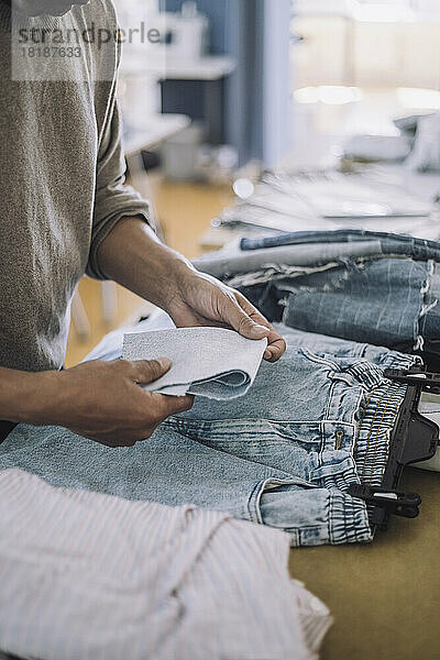 Männlicher Modedesigner faltet Stoff mit Jeans auf einer Werkbank in einer Werkstatt
