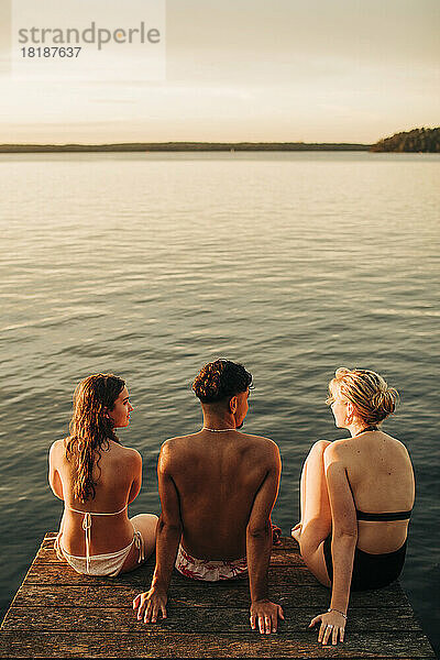 Hohe Winkel Ansicht der männlichen und weiblichen Freunde sitzen auf Steg am See im Urlaub