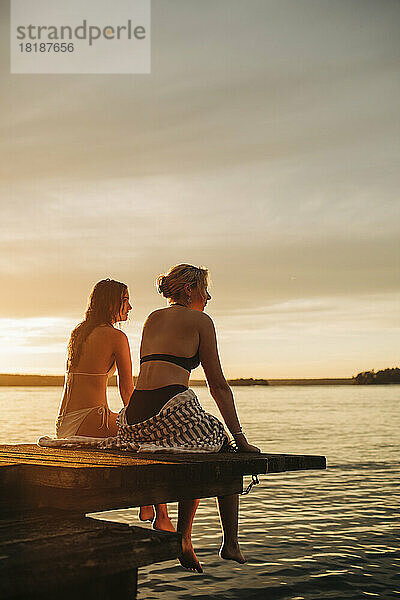 Frauen sitzen bei Sonnenuntergang auf einem Steg am See