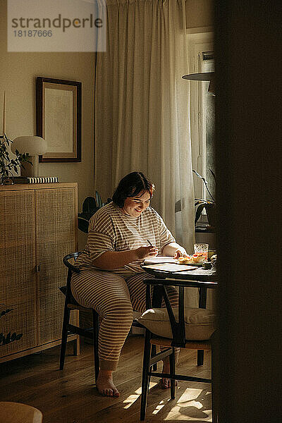Lächelnde junge Frau  die am Tisch sitzend schreibt