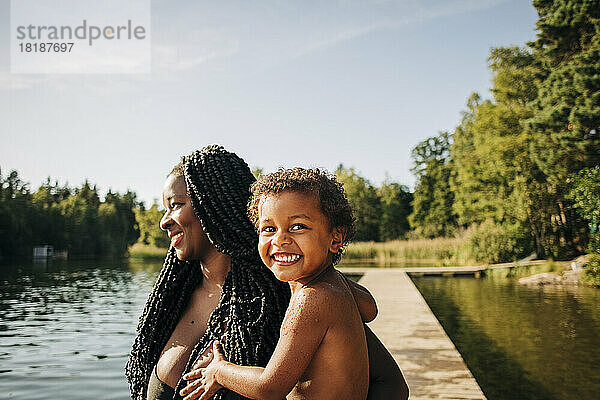 Lächelnde Frau mit aufgeregtem Sohn am See im Urlaub