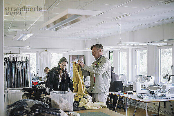 Männliche und weibliche Design-Profis sortieren in der Werkstatt recycelte Kleidung aus