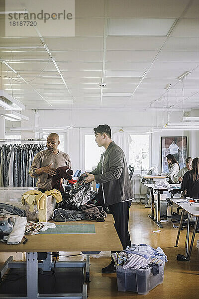 Männliche Design-Profis sortieren in einem Workshop recycelte Kleidung