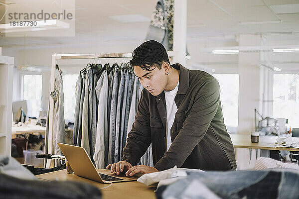 Konzentrierter männlicher Modedesigner mit Laptop in der Werkstatt