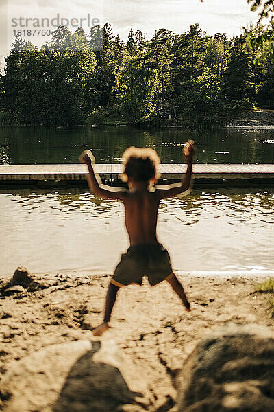 Rückansicht eines Jungen  der im Urlaub auf einen Felsen am See springt