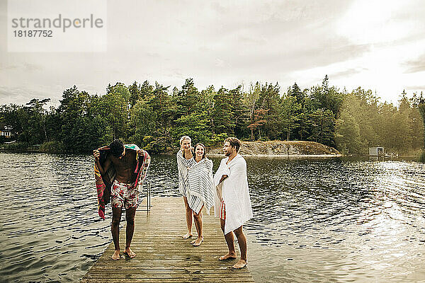 Glückliche Freunde  die ein Handtuch tragen  während sie im Urlaub auf dem Steg am See stehen