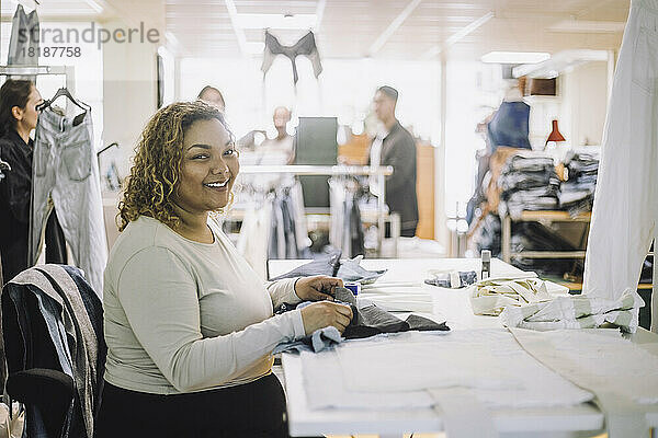 Porträt einer lächelnden Modedesignerin  die an einer Werkbank in einer Werkstatt sitzt