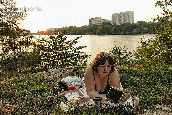 Junge  üppige Frau liest ein Buch  während sie am See liegt