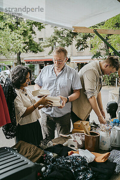 Älterer männlicher Besitzer  der einer Kundin beim Kauf von Büchern auf dem Flohmarkt hilft