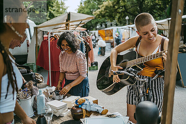 Lächelnde Kundin spielt Gitarre beim Einkaufen auf dem Flohmarkt