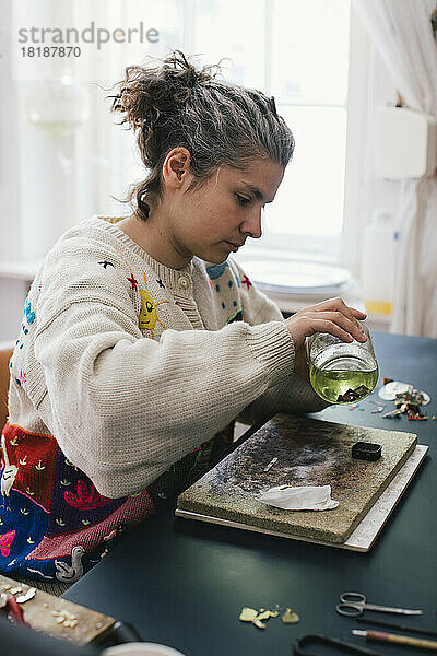 Weibliche Kunsthandwerkerin hält einen Krug  während sie zu Hause Schmuck herstellt